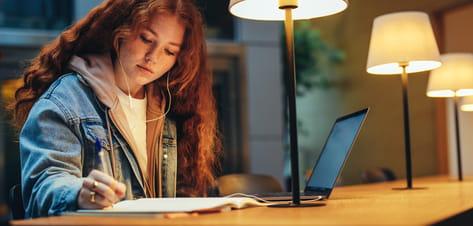 A female student studies in the evening at the university library with lamps on the desk